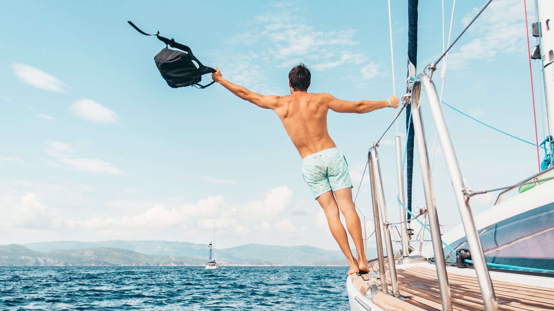 Hombre sujetando una mochila subido a un barco