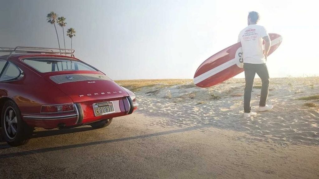 Hombre con tabla de surf y Porsche 911 rojo