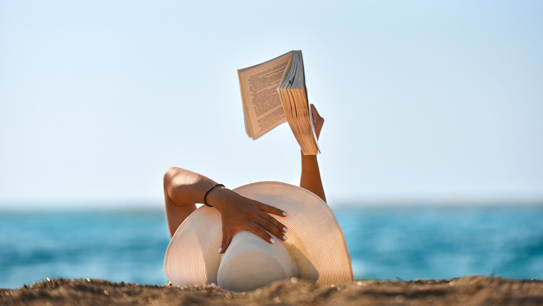 Mujer leyendo con pamela en la playa