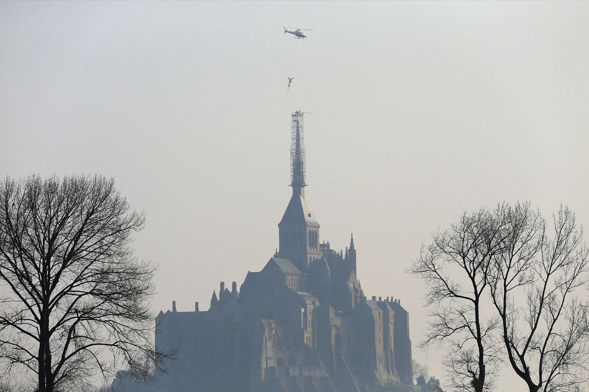 Imagen del momento en el que un helicóptero retira la estatua del arcángel San Miguel en la abadía que lleva su nombre, en Normandía. (AFP)