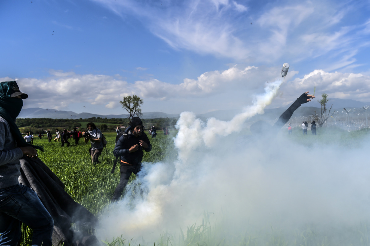 Un grupo de refugiados en Idomeni se defiende de la policía que lanza botes de gas lacrimógeno. (Foto: AFP)