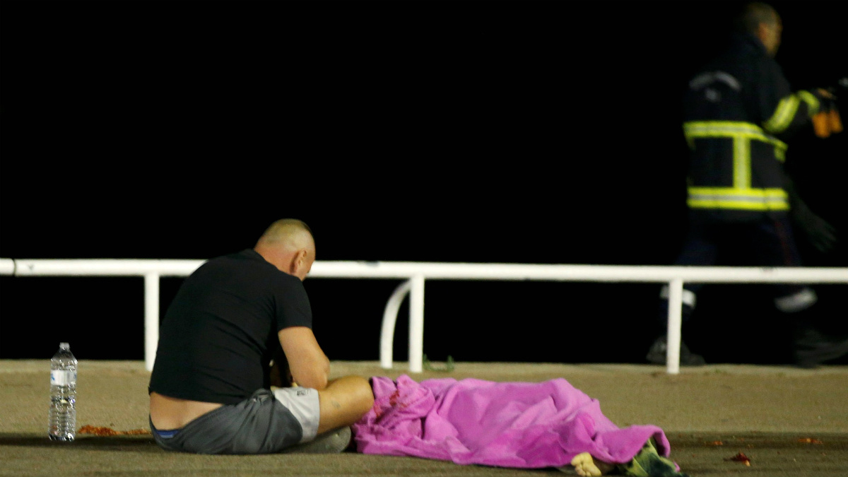 Un superviviente vela uno de los cuerpos tapado por una manta rosa, tras el atentado de Niza. (Reuters)