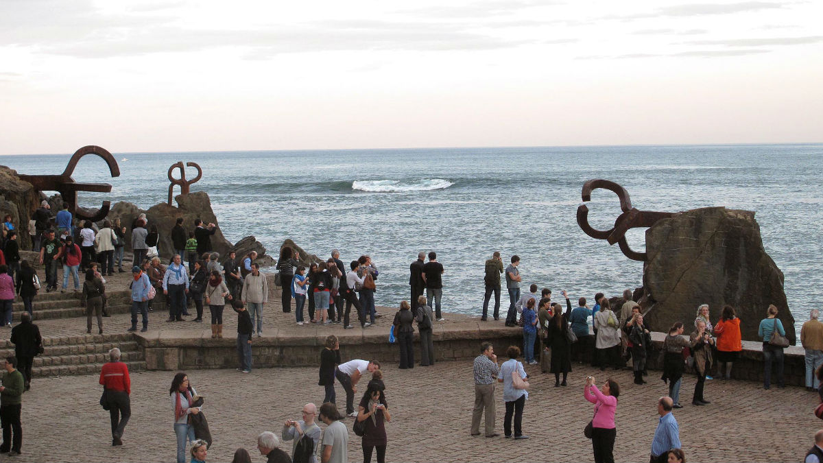 Transeúntes disfrutan del conjunto escultórico ‘El Peinde del Vieno’, de Chillida, en uno de los extremos de la bahía de La Concha. (Foto: CC)