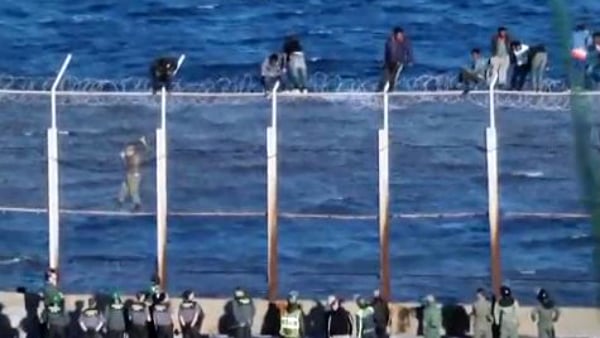 Inmigrantes encaramados a la verja fronteriza de Ceuta, con el mar al fondo.