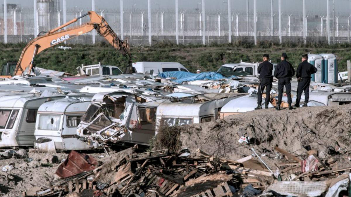 Tres agentes de seguridad observan la demolición de parte del campamento de refugiados francés conocido comom ‘La Jungla’ de Calais. AFP