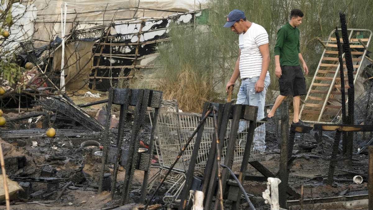 Inmigrantes buscan entre los restos de su chabola arrasada por el fuego, en Lepe. (EFE)