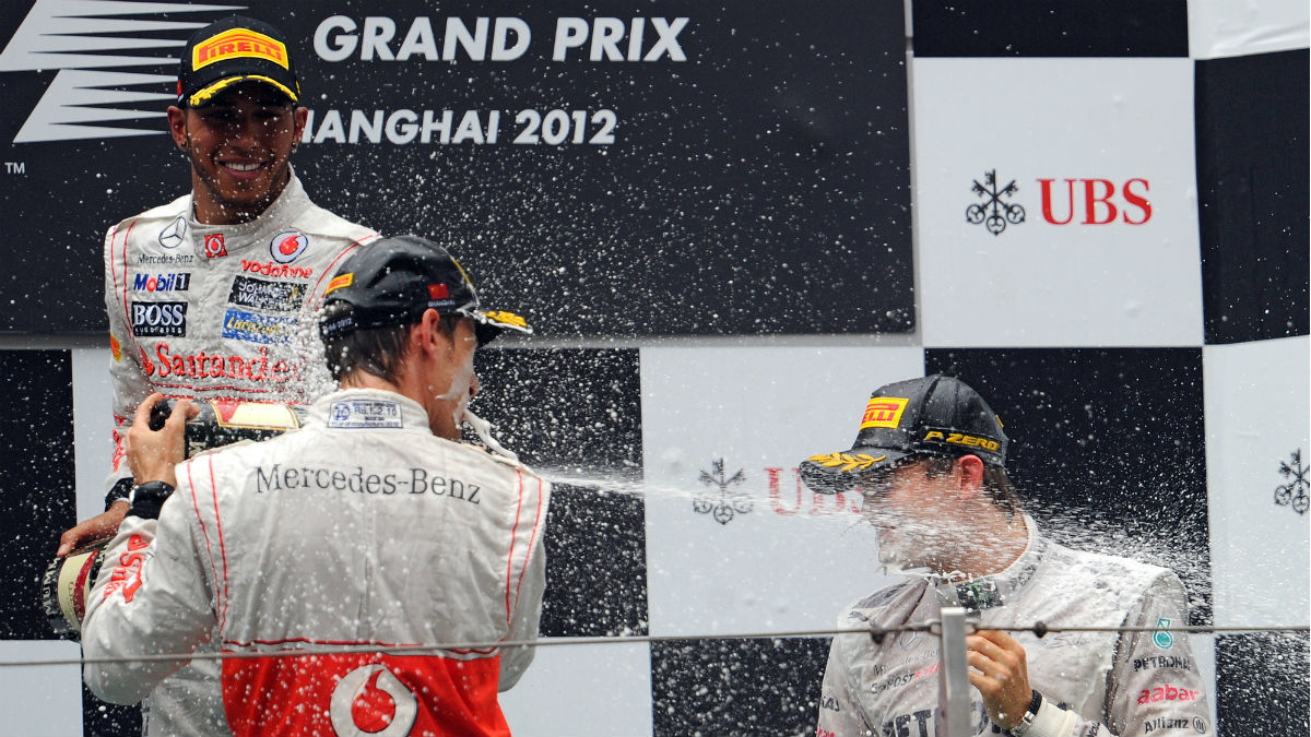 Jenson Button lanza champán a la cara de Nico Rosberg con Hamilton de testigo. (AFP)