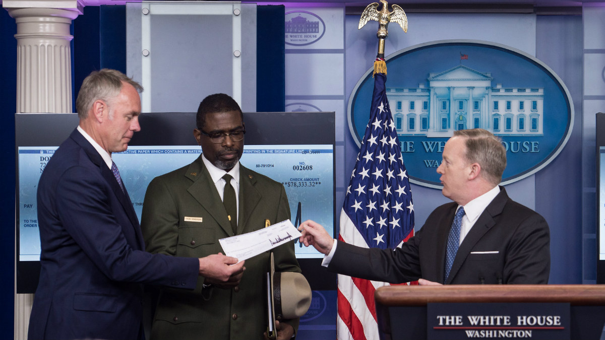 El portavoz de la Casa Blanca, Sean Spicer, entrega al secretario de Interior, Ryan Zinke, el primer cheque del salario del presidente de Estados Unidos, Donald Trump, donado al Servicio Nacional de Parques (Foto: AFP)