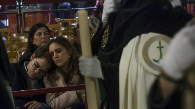 Una pareja descansa mientras los nazarenos de la Esperanza de Triana pasan por la Carrera Oficial, esta noche durante la Madrugá de Sevilla. Foto: EFE