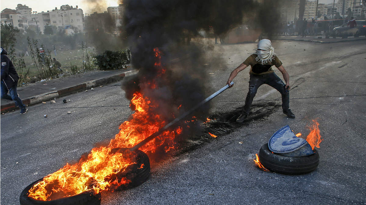 Un radical palestino mueve neumáticos ardiendo con una barra de hierro en el checkpoint de Qalandia, en las afueras de Ramala (Cisjordania). (AFP)