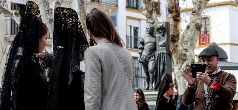 Un turista fotografía a unas jóvenes vestidas de mantilla junto la Basílica de Nuestro Padre Jesús del Gran Poder, antes de salir en procesión en la Madrugá sevillana. Foto: EFE