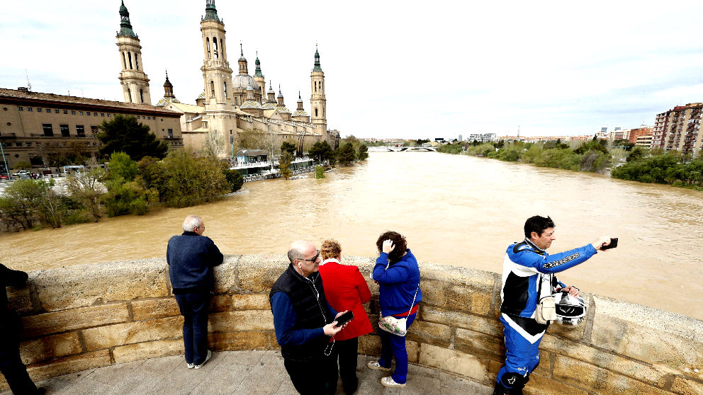 Varias personas observan el paso del río Ebro por el Puente de Piedra de Zaragoza (Foto: Efe).