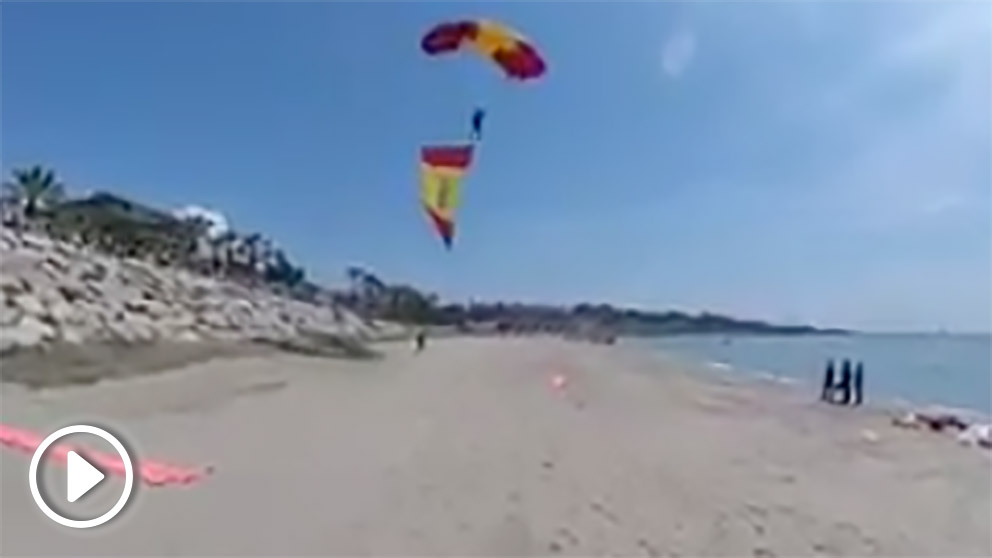 Paracaidista aterrizando con una bandera de España en una playa de Tarragona