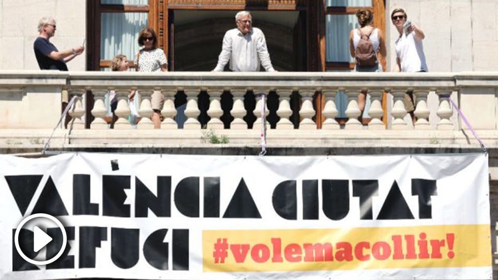El alcalde de València, Joan Ribó (c) , se asoma al balcón de la Plaza del Ayuntamiento tras la instalación de una gran pancarta con el lema «Valencia, ciudad refugio». (Foto: Efe)