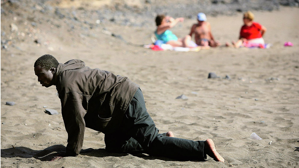 Un inmigrante llegado en patera a las costas españolas se arrastra por la playa ante unos bañistas. (EP)