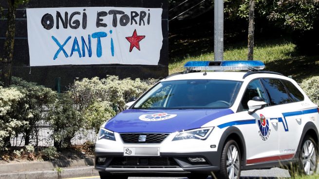 Una patrulla de la Ertzaintza pasa delante de una pancarta en homenaje al etarra Santi Potros. (Foto: EFE)