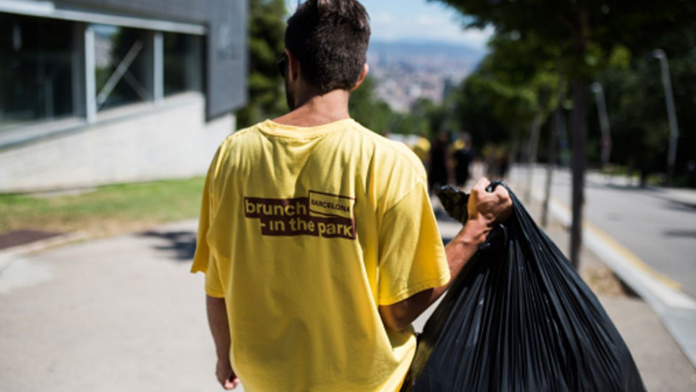 Un voluntario con una camiseta de Brunch In The Park con una bolsa de basura.