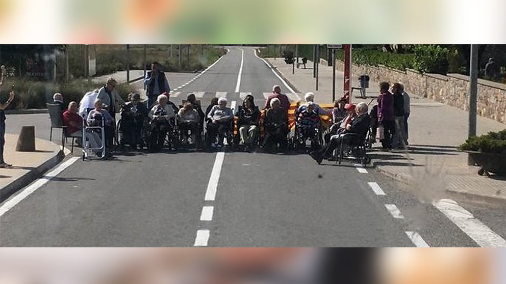 Varios ancianos en silla de ruedas cortando una carretera con motivo del 1-O