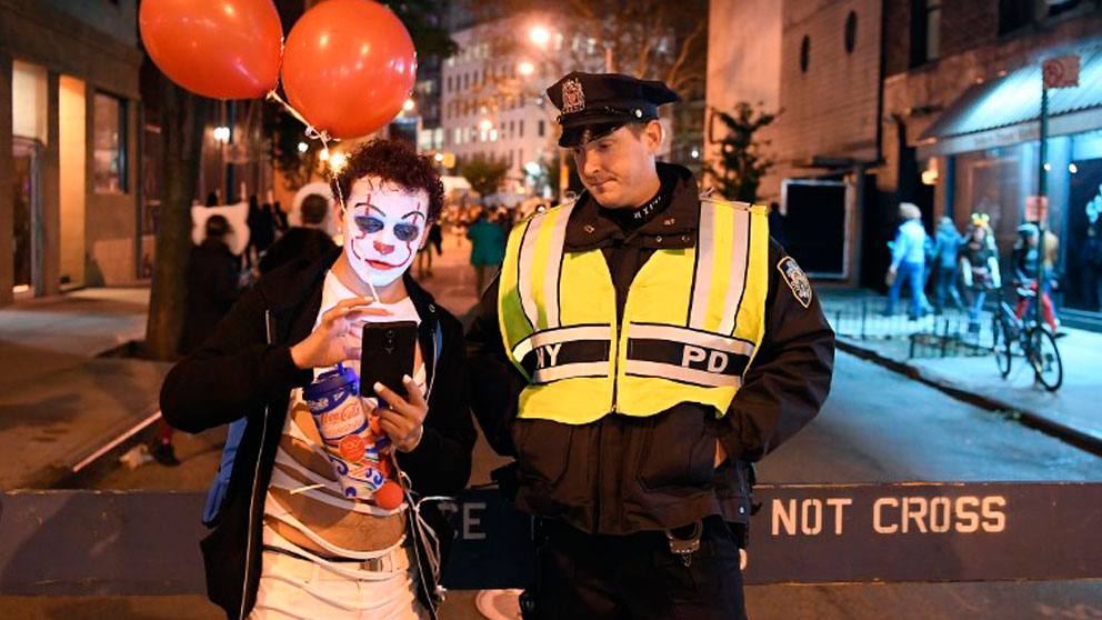 Un hombre disfrazado de payaso junto a un Policía de Nueva York celebrando la festividad pagana de Halloween. Foto. AFP