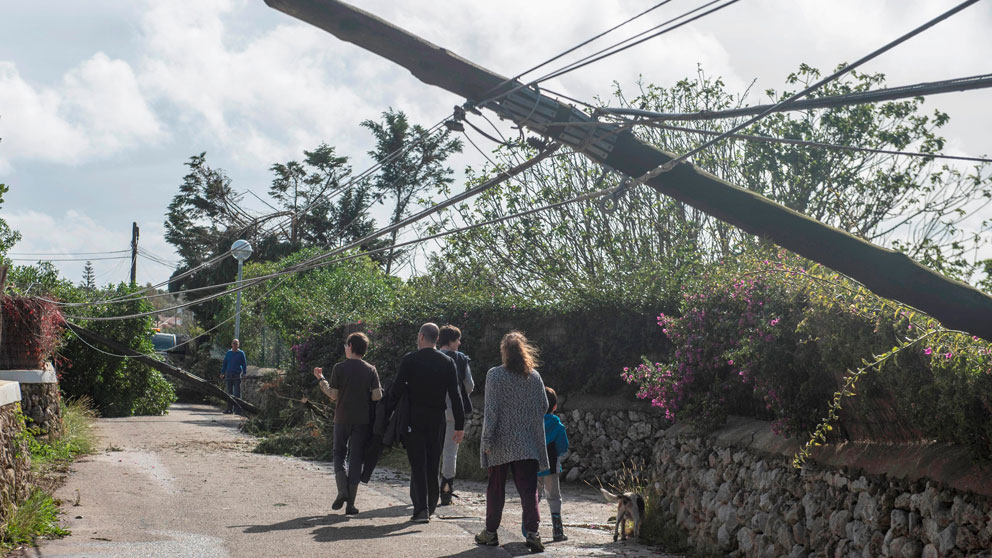 Vecinos de Menorca pasean junto a unos postes de electricidad caídos. Foto: EFE
