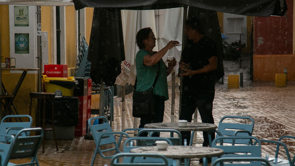 DOs personas se refugian de la lluvia bajo la sombrilla de un bar. Foto: EP