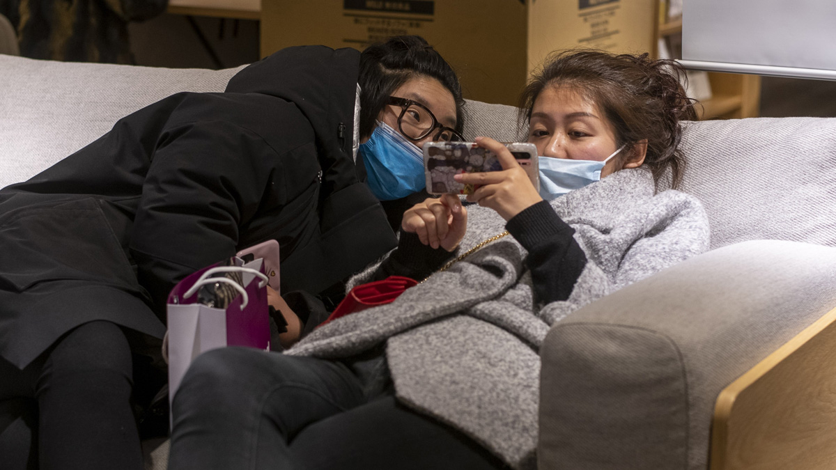Dos ciudadanos chinas ven el móvil ataviadas con mascarillas en una tienda de Hong Kong. Foto: EP