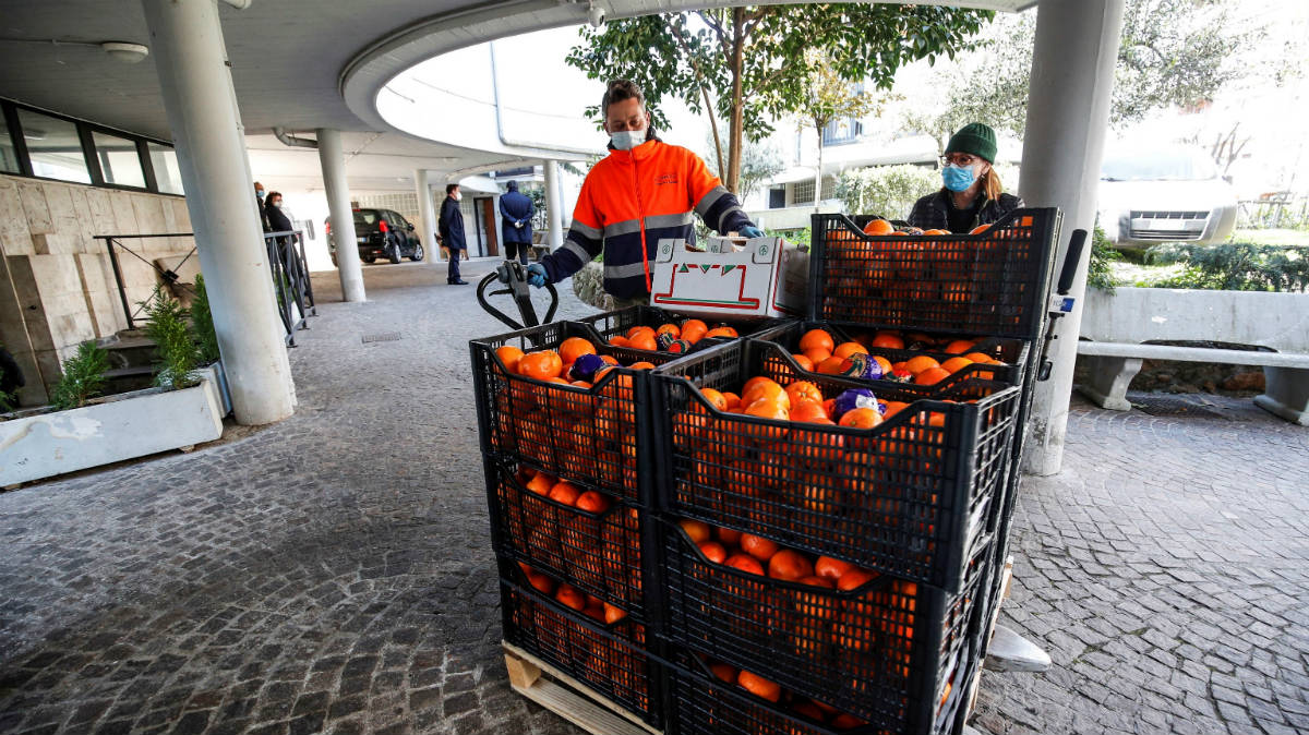 Operarios protegidos por mascarillas manipulan un cargamento de fruta en un mercado de Roma (Foto: EFE).