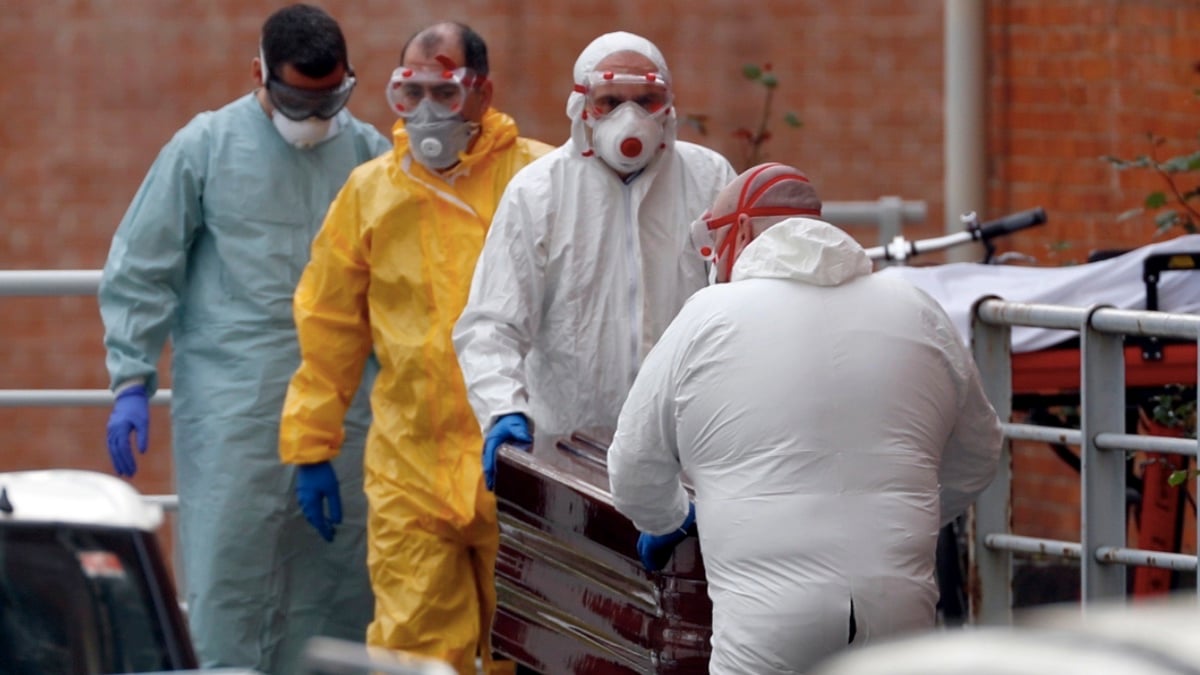 Trabajadores de una funeraria protegidos trasladan de la morgue a un fallecido por coronavirus. (Foto: EFE)