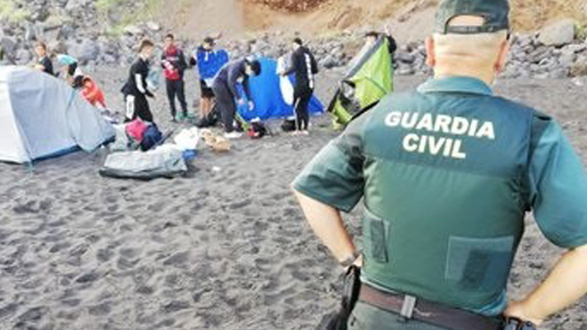 Un agente de la Guardia Civil vigila como los 62 campistas que habían quedado para propagar el coronavirus abandonan la playa de Los Patos en Tenerife. Foto: EP