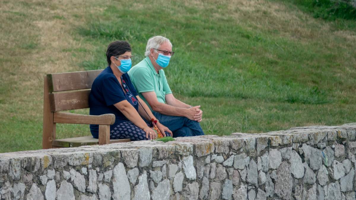 Una pareja sentada con mascarillas en _el banco más bonito del mudo_ en LLanes. Foto: EP