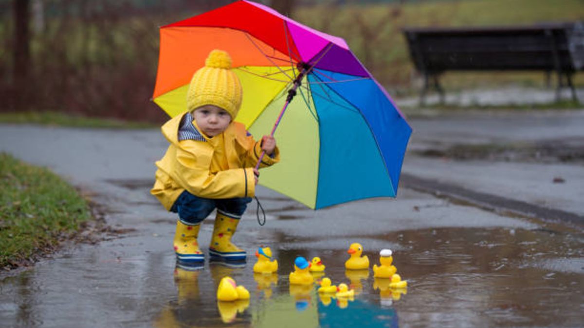 Niño con capa impermeable amarilla y botas jugando al aire libre