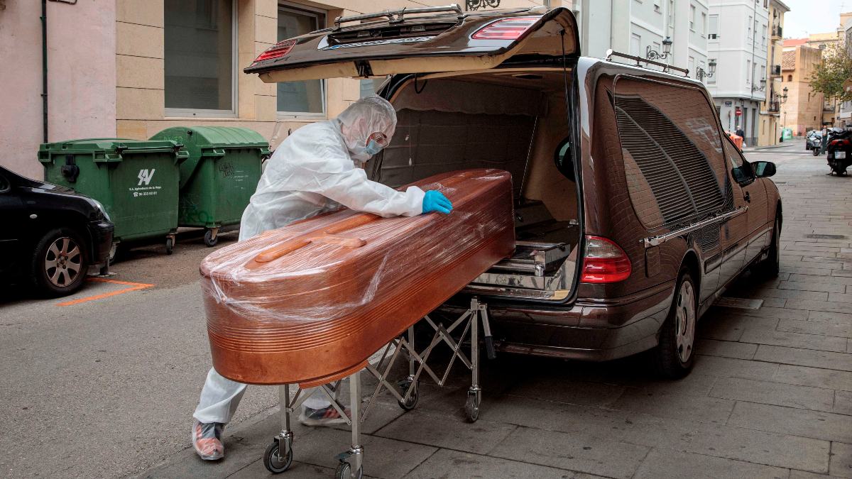 Un operario de una funeraria con un EPI anti-coronavirus introduce un ferétro en el coche fúnebre. (Foto: Efe)