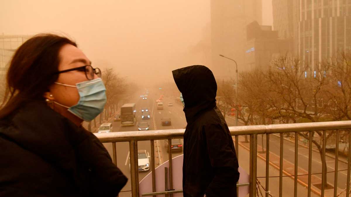 Ciudadanos caminan por una pasarela exterior con la tormenta de arena y polución de fondo en Pekín. Foto: AFP