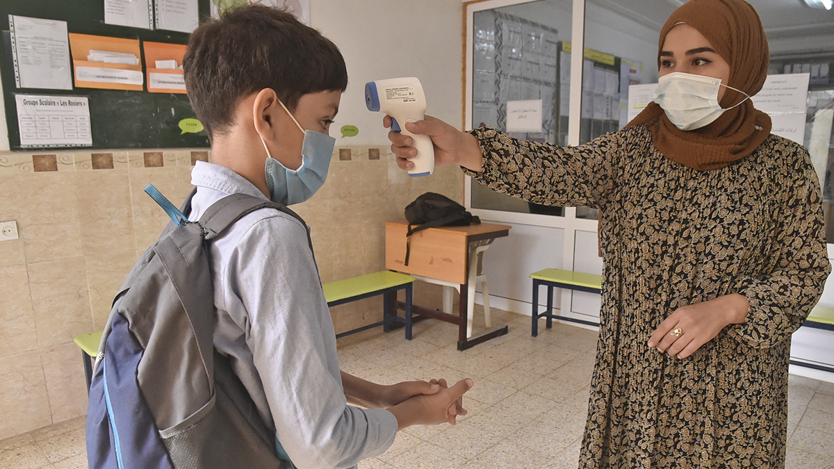 Una profesora toma la temperatiura a un alumno en un colegio de Argel.