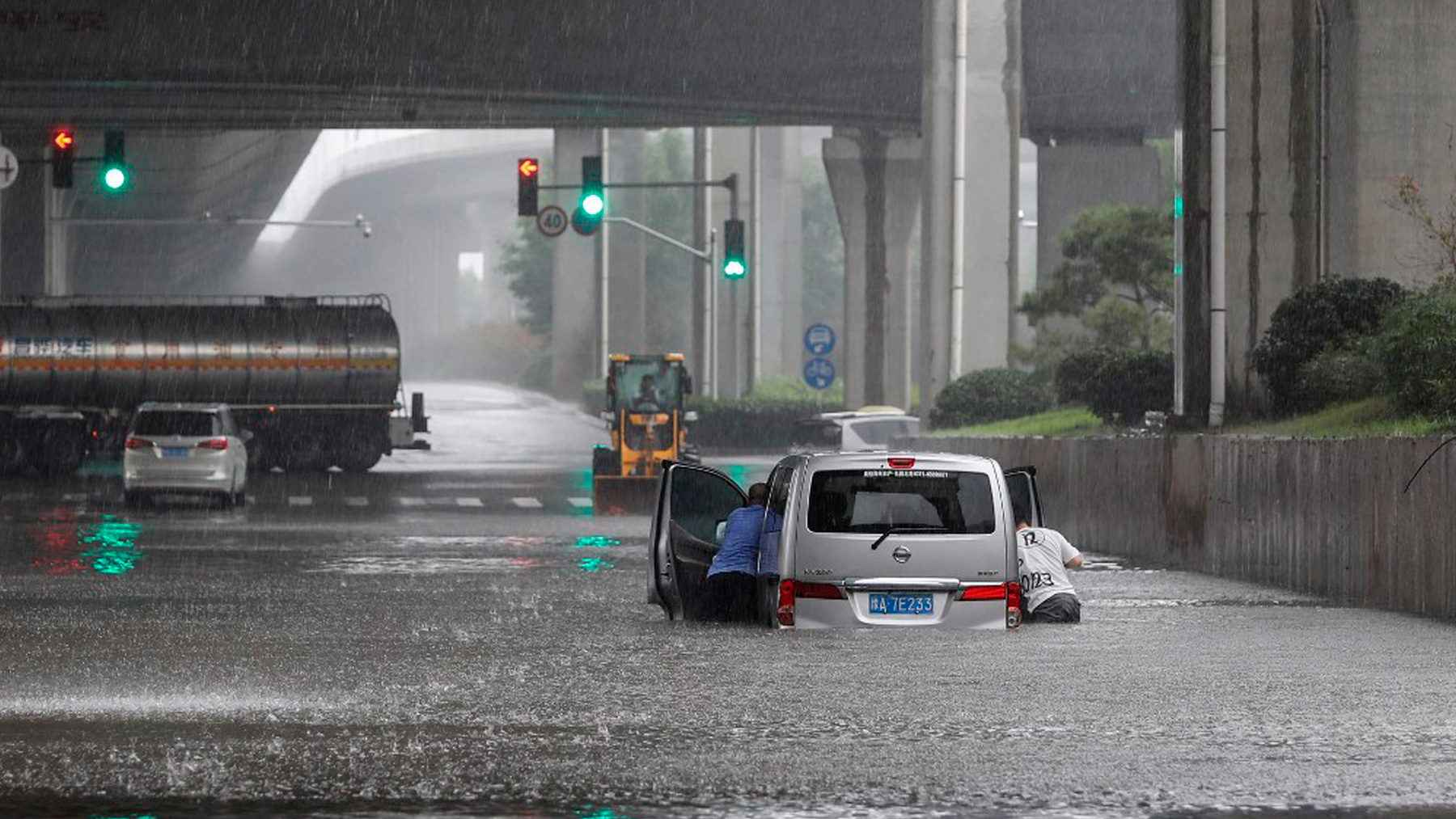 Dos personas tratan de sacar su coche de la inundación provocada por las lluvias en la provincia china de Henan. Foto: AFP