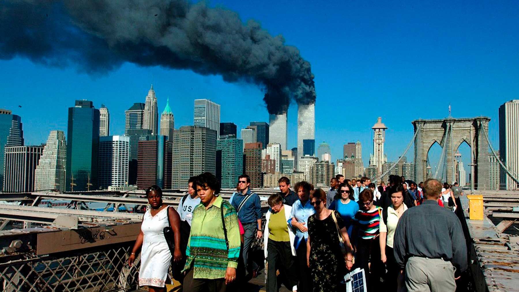 Un grupo de personas camina por el puente de Brooklyn en Nueva York con las Torres Gemelas ardiendo antes de derrumbarse detrás. Foto: AFP