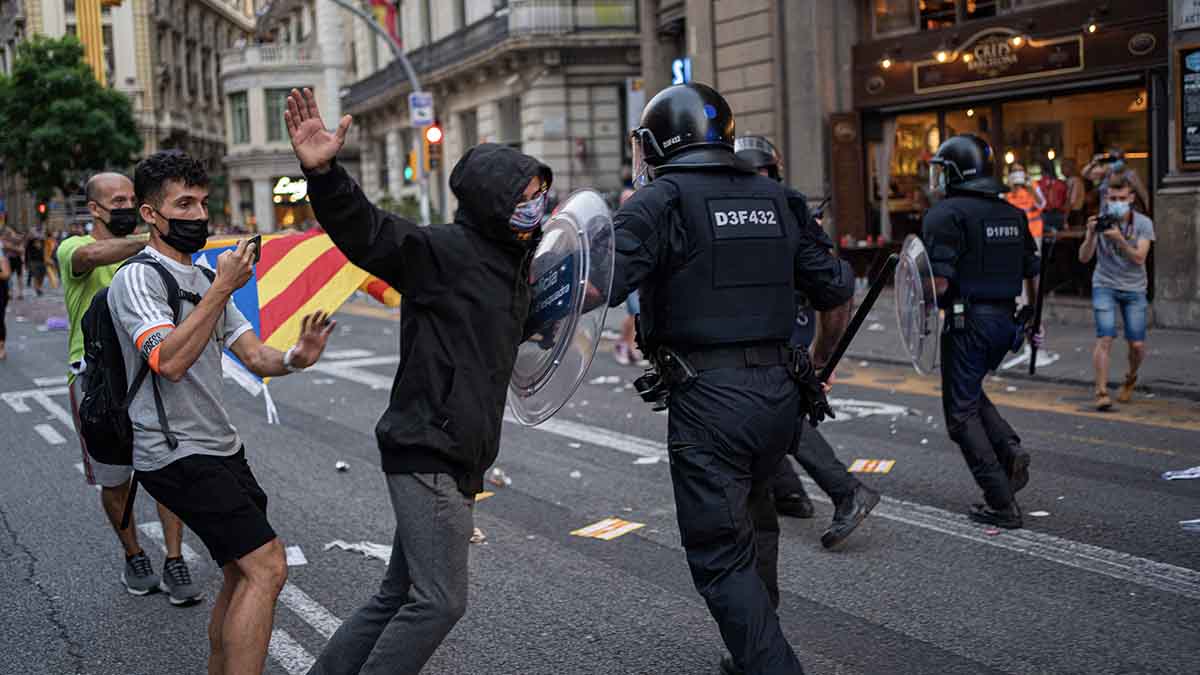 Un Mosso carga contra un hombre durante los altercados en la comisaría de la Policía Nacional