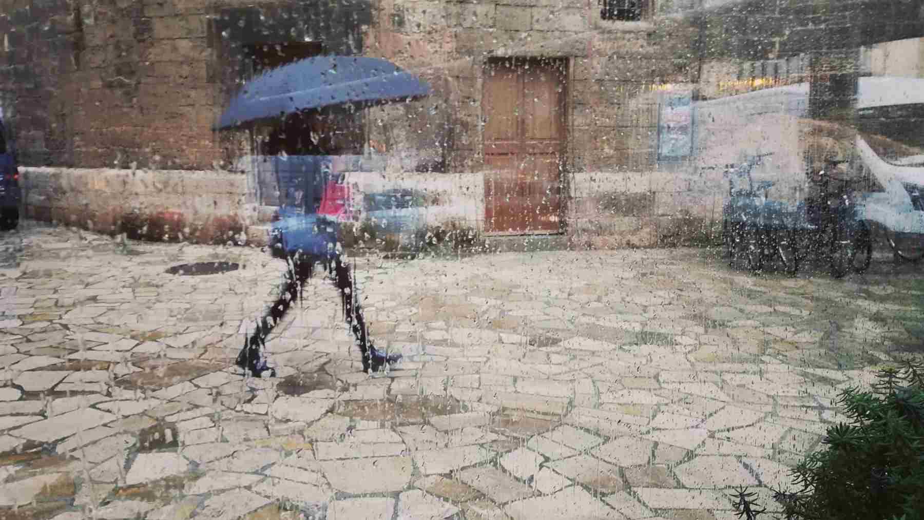 Una mujer pasea por el centro de Palma con un paraguas, vista a través de un cristal con gotas de lluvia. Foto: Europa Press