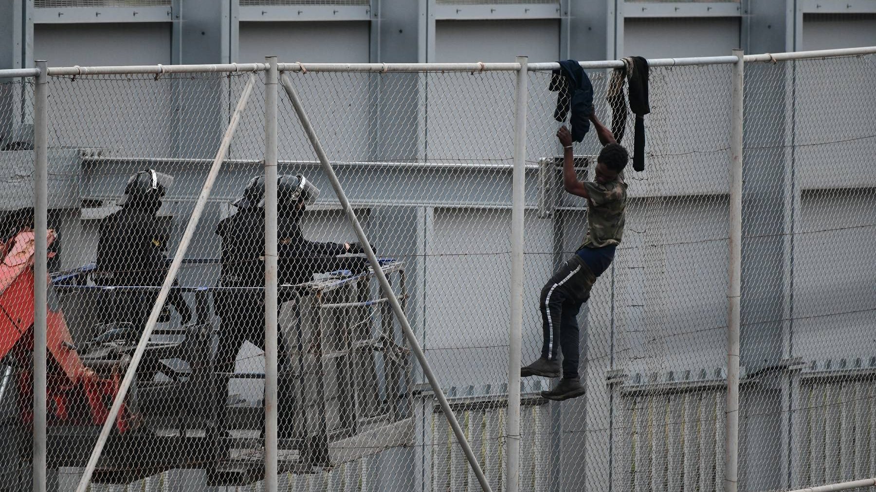 Tres agentes se acercan a un inmigrante ilegal que intenta saltar la valla de Ceuta (ANTONIO SEMPERE / EUROPA PRESS). (1) (1)