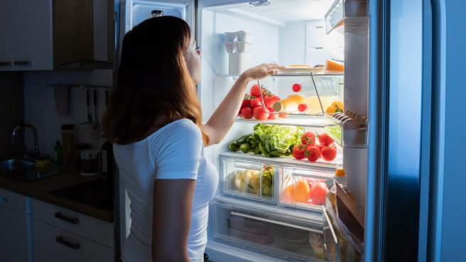 Mujer buscando dentro de un frigorífico con la puerta abierta