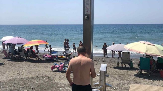Un usuario de la playa de Algarrobo (Málaga) junto a una de las duchas de la playa.