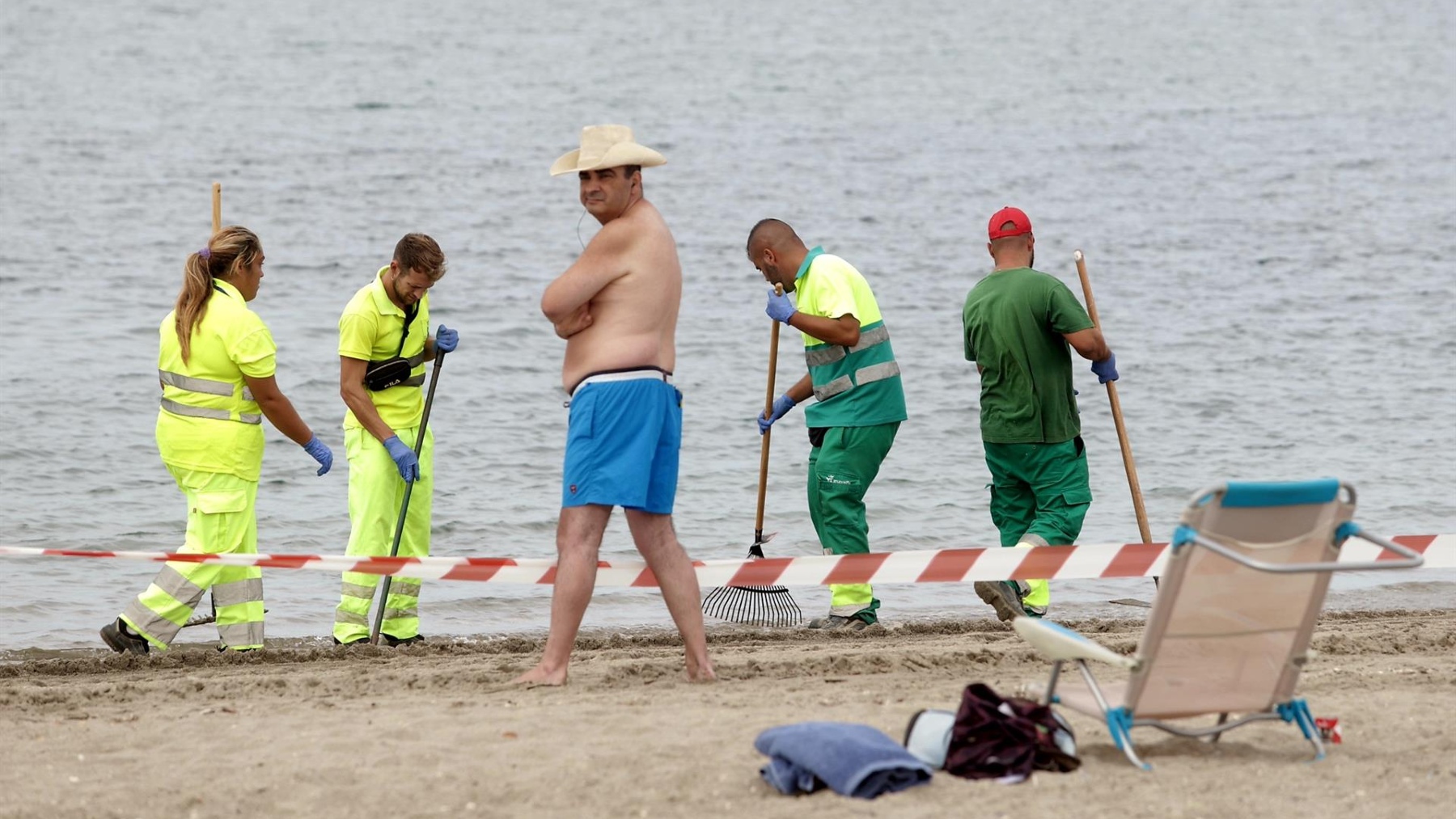 Un bañista en la playa de Poniente de La Línea mientras los operarios retiran restos del vertido (EUROPA PRESS).