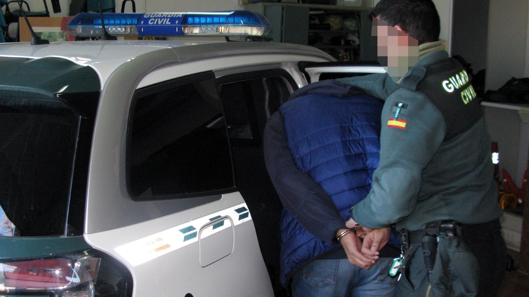 Un agente de la Guardia Civil introduce a un detenido en un vehículo patrulla.