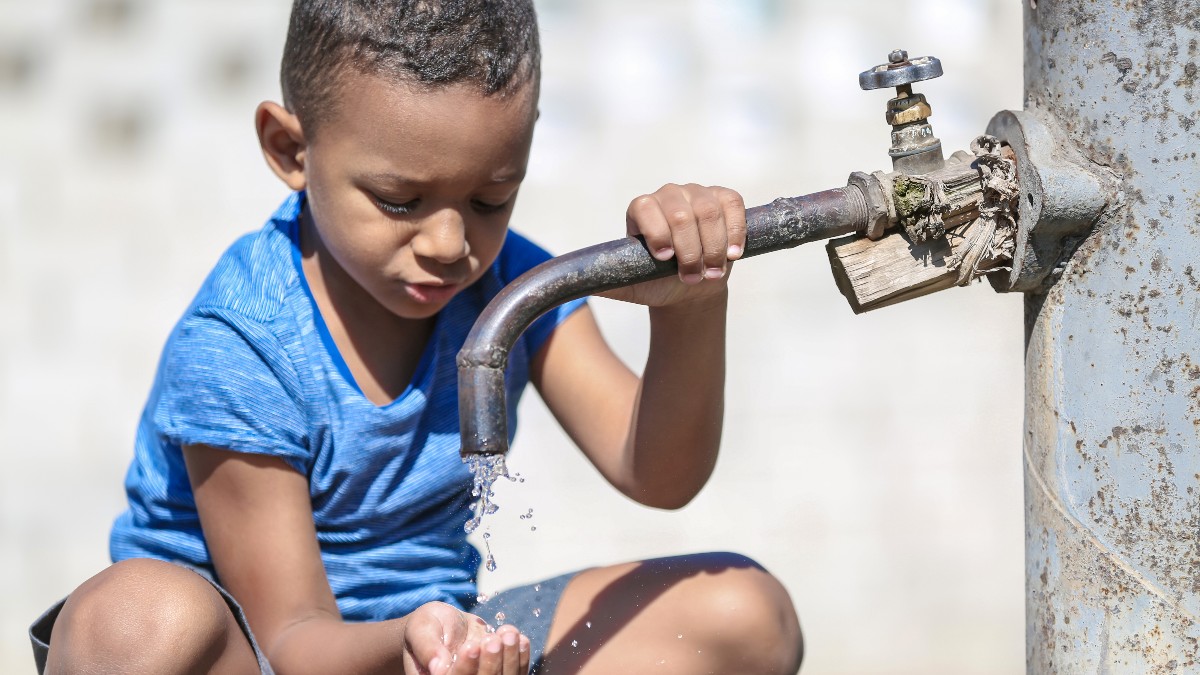 Niño bebiendo agua del grifo al aire libre. Escasez de agua en África.