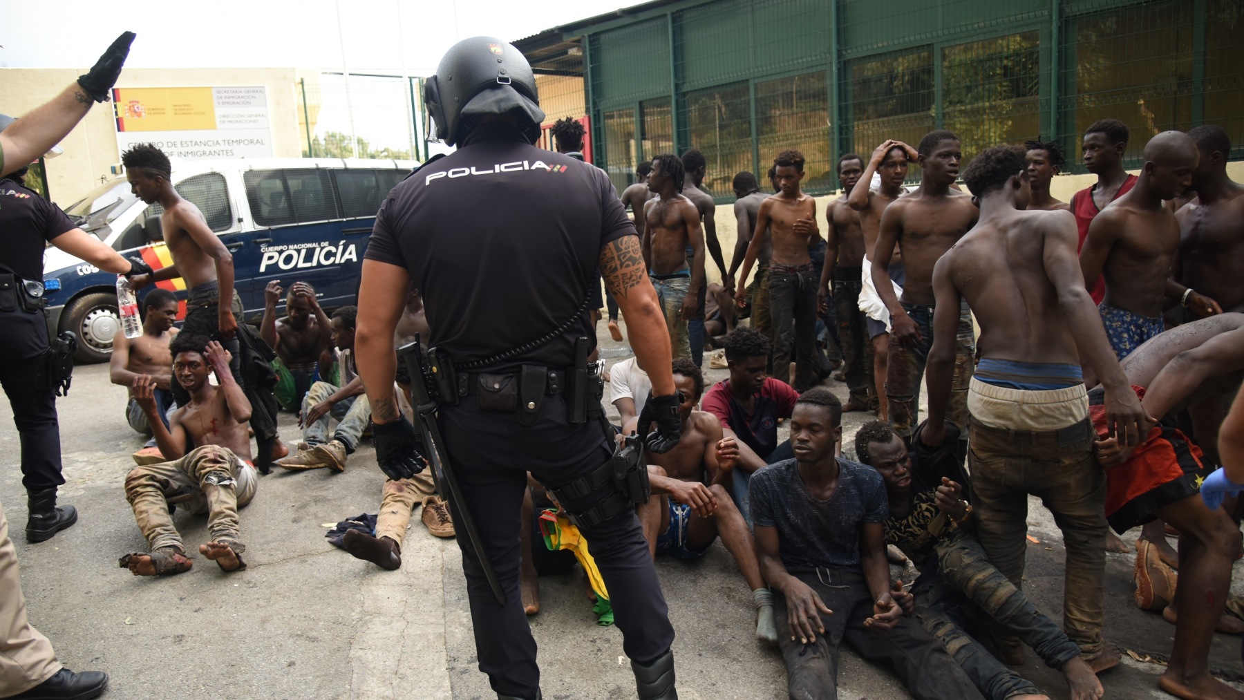 Un policía nacional frente a un grupo de inmigrantes ilegales llegados a Ceuta.