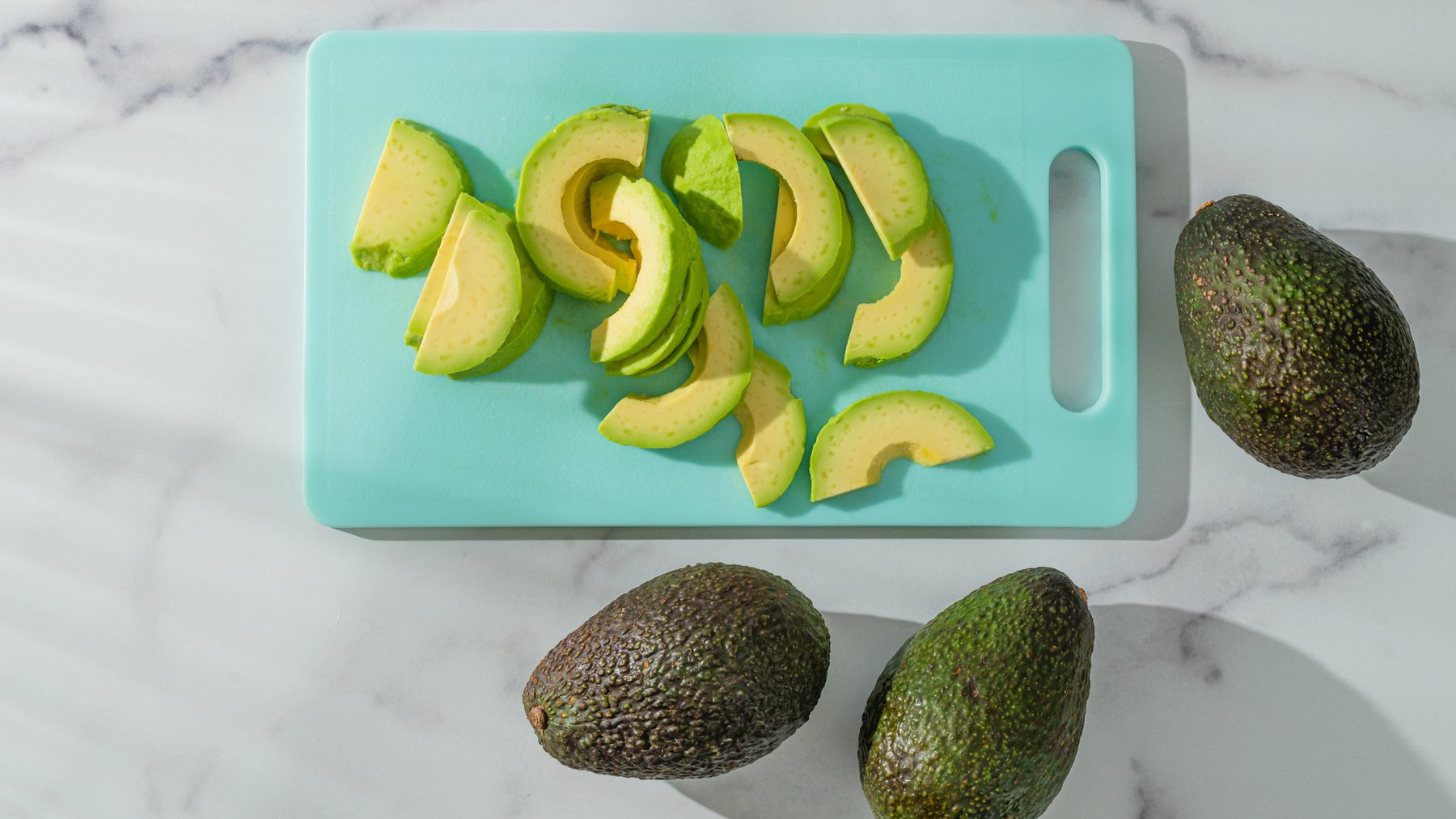 Avocado close-up on the kitchen table. Fresh sliced avocado on a cutting board on a marble background