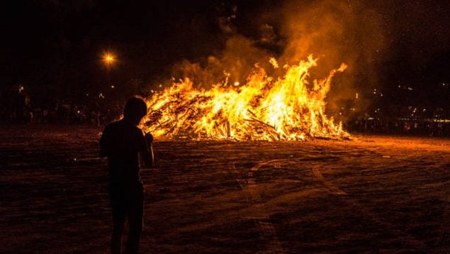 Foto de una hoguera de San Juan de gran tamaño con una persona delante.