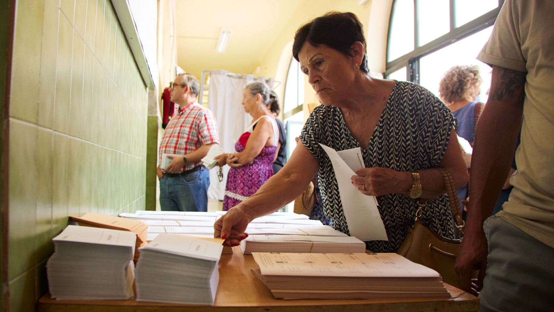 Una señora coge una papeleta de una mesa electoral este 23J en Sevilla (EUROPA PRESS).