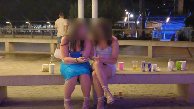 Dos chicas sentadas de noche en una plaza de Magaluf con bebidas alrededor