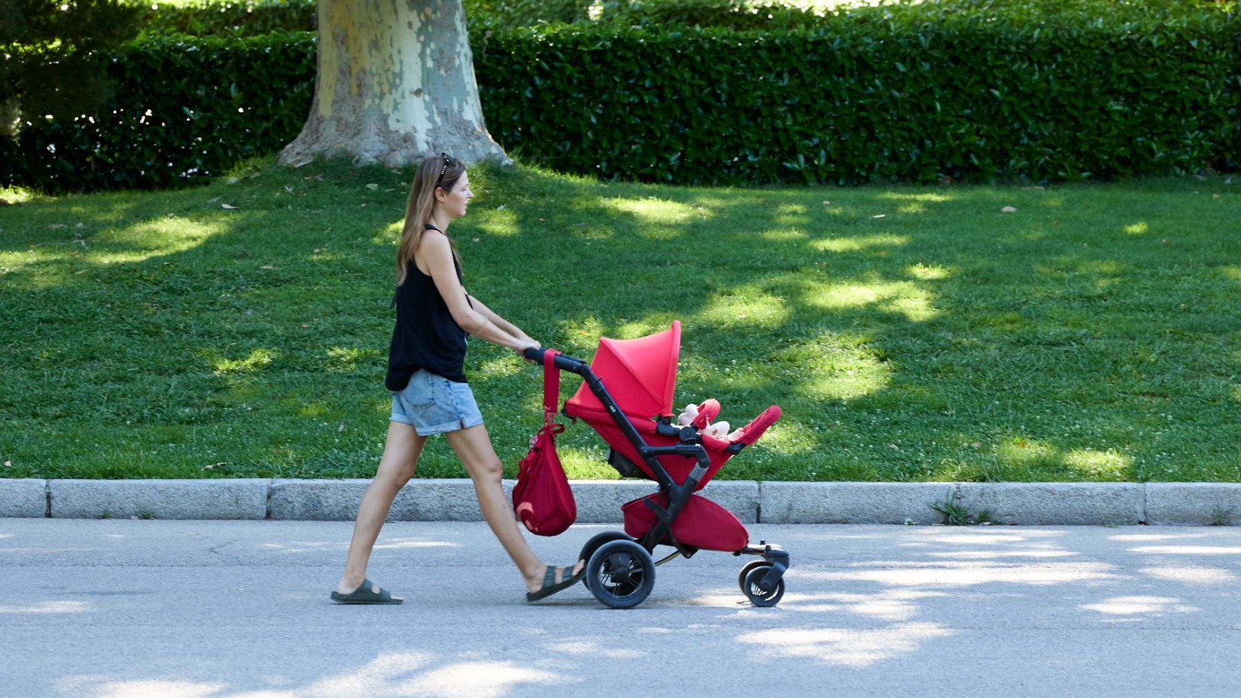 Una mujer pasea con su hijo por un parque de Madrid.